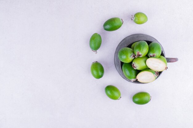 Green feijoas in a metallic pot on grey surface