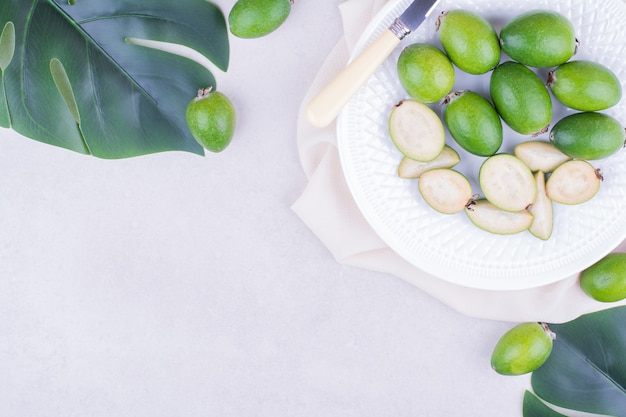 Feijoas verdi in un piatto bianco con foglie intorno.