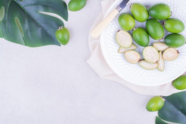 Green feijoas in a white platter with leaves around.