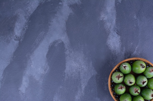 Green feijoas in a wooden cup on blue surface