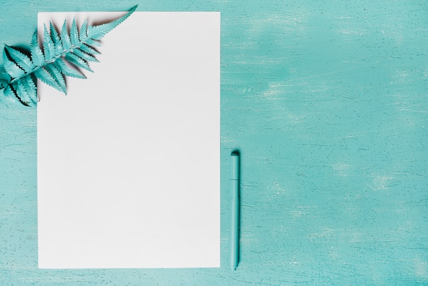 Free photo green fern leaves on paper and pen against turquoise background