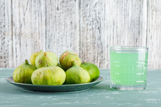 Free photo green figs in a plate with drink side view on plaster and wooden table