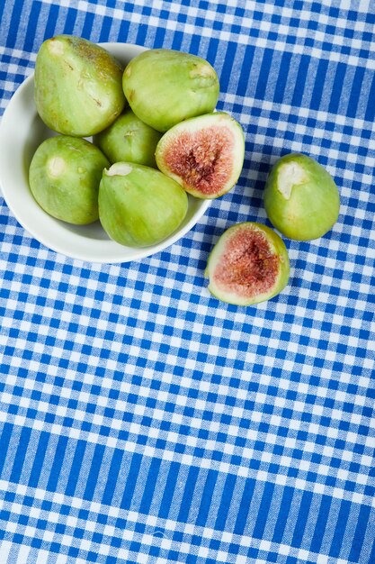 Green figs in a white bowl and on a blue tablecloth