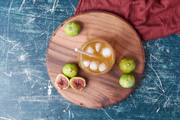 Fichi verdi con una tazza di bevanda sull'azzurro.