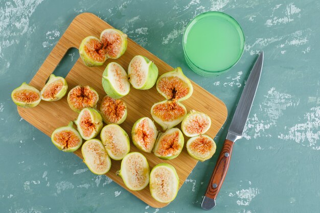 Green figs with drink, knife flat lay on plaster and cutting board