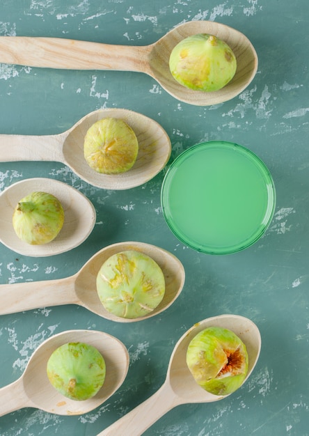 Free photo green figs with drink in wooden spoons on plaster wall, top view.