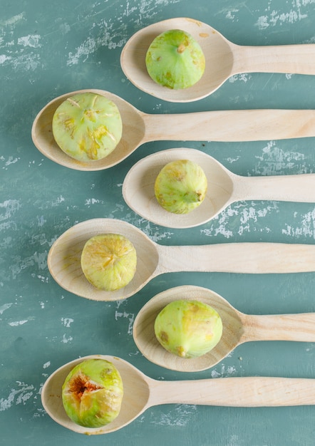 Free photo green figs in wooden spoons on plaster wall, flat lay.