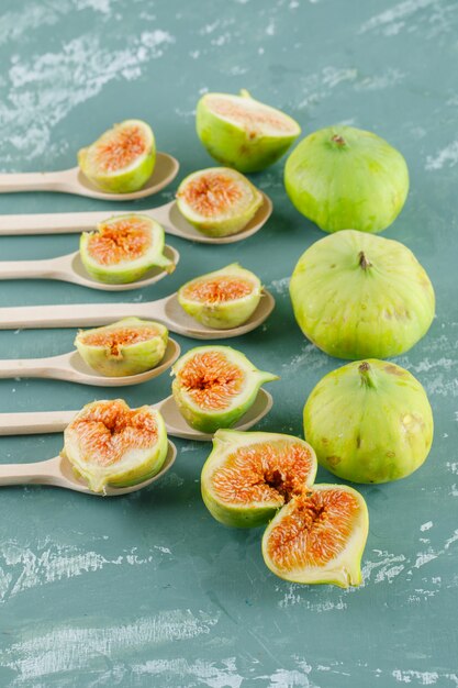 Free photo green figs in wooden spoons on a plaster wall. top view.