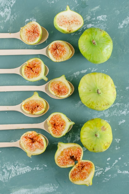 Green figs in wooden spoons top view on a plaster wall