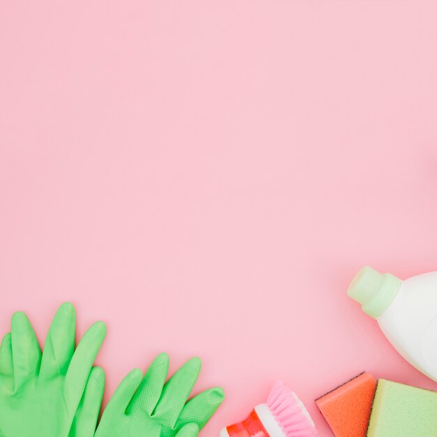 Green gloves; spray bottle; sponge and detergent bottles on yellow backdrop