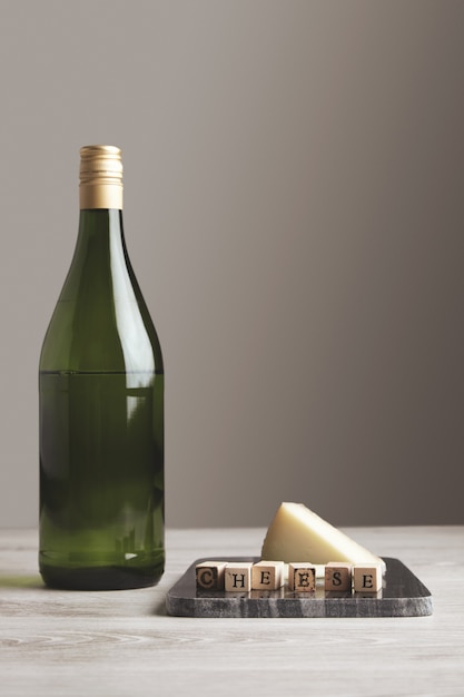 白い空白の背景とテーブルに分離された木製の文字チーズと山羊のチーズと石の大理石のボードの近くに緑ブドウワインジュースボトル