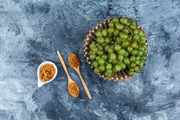 Green grapes in a basket with raisins flat lay on a grungy plaster background