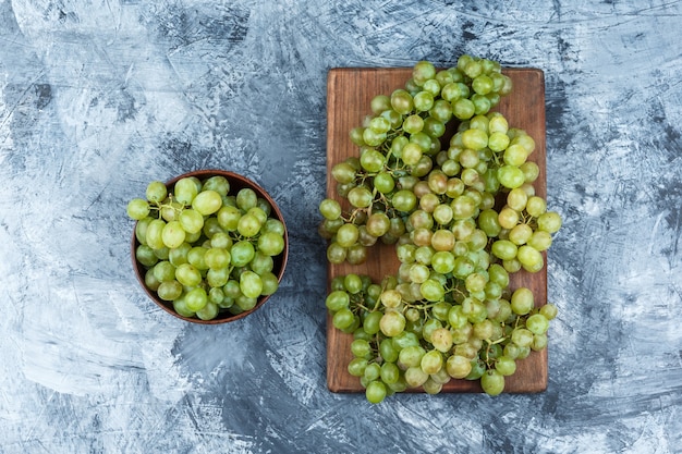 ボウルフラットの緑のブドウは、汚れた石膏とまな板の背景に横たわっていた