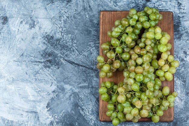 Green grapes on grungy plaster and cutting board background. flat lay.