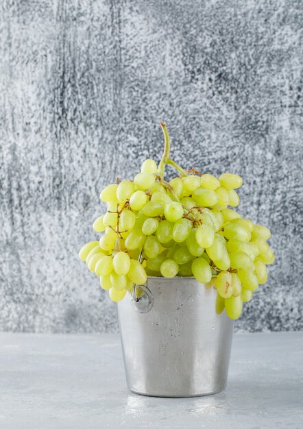 Зеленый виноград в мини-ведре, вид сбоку на штукатурке и шероховатый серый