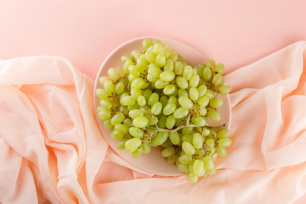 Foto gratuita l'uva verde in un piatto piatto giaceva sul rosa e sul tessuto