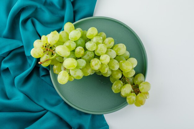 Green grapes in a plate flat lay on white and textile