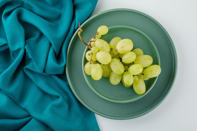 Green grapes in a saucer with plate flat lay on white and textile