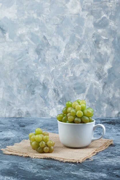 Green grapes in a white cup side view on grunge and piece of sack background