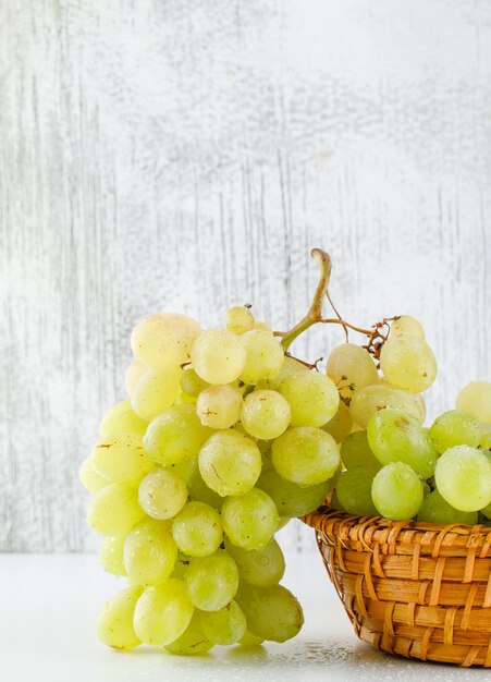 Green grapes in a wicker basket on white and grungy, close-up.