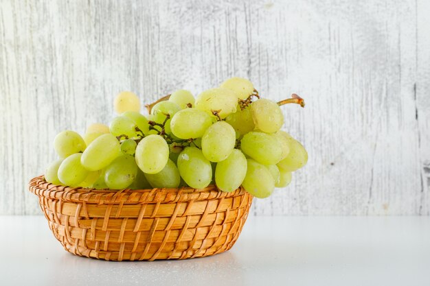 Green grapes in a wicker basket on white and grungy.