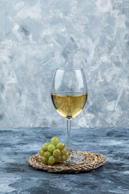 汚れた石膏と枝編み細工品のプレースマットの背景にワインの側面図のガラスと緑のブドウ