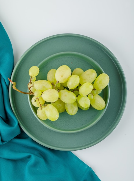 Green grapes with plate in a saucer on white and textile,