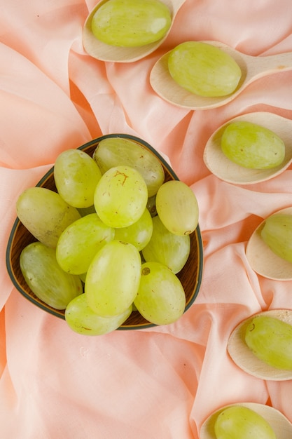 Green grapes in wooden spoons and bowl on pink textile,