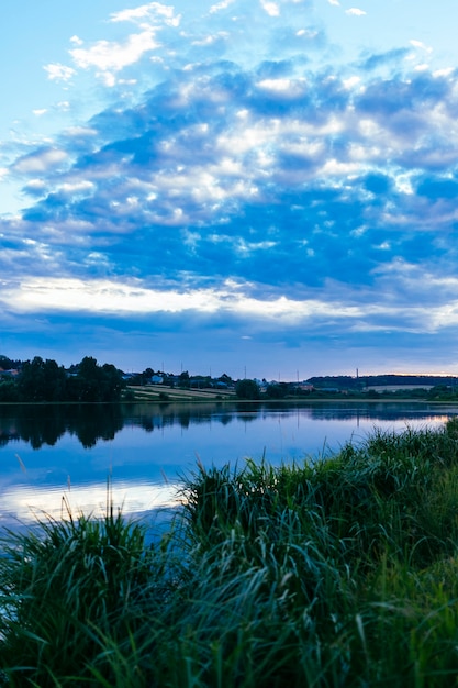 Green grass over the idyllic lake with blue dramatic sky