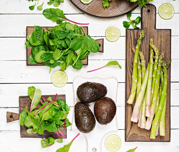 Green herbs, asparagus and black avocado on a white wooden background. Top view. Flat lay