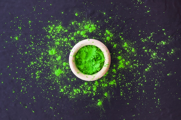 Green holi powder in bowl on textured background