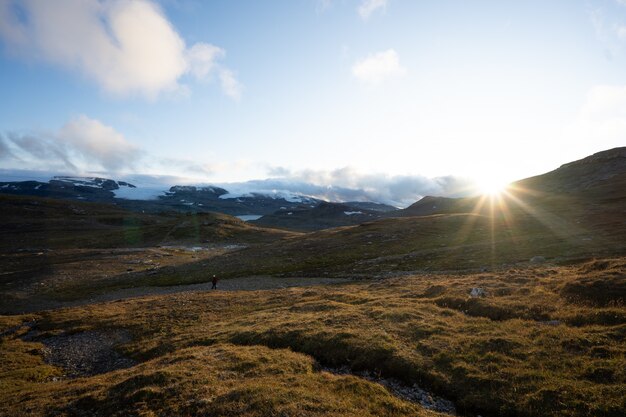 노르웨이 Finse의 배경에 밝은 태양이있는 높은 록키 산맥으로 둘러싸인 녹색 땅