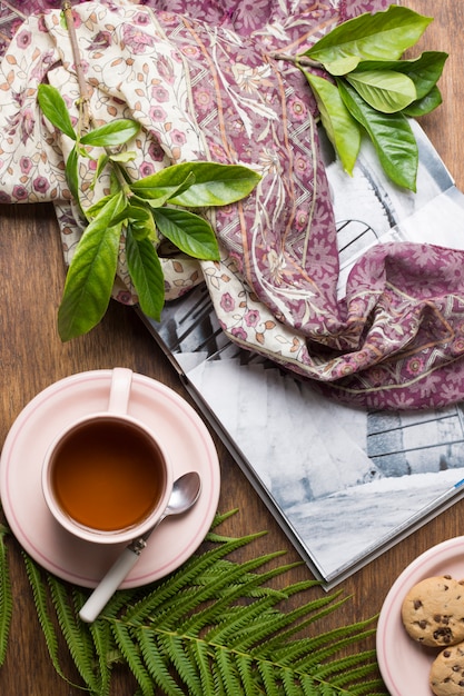 Foto gratuita foglie verdi sul libro; tazza di tè e biscotti sul tavolo di legno