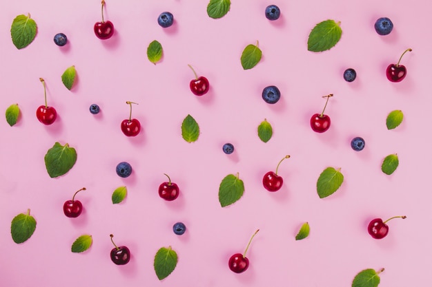 Green leaves, cherries and blueberries on pink surface