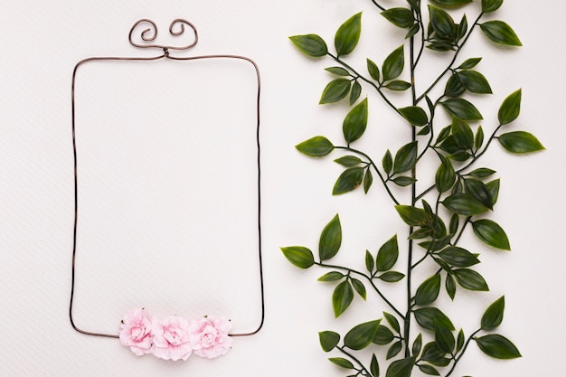 Free photo green leaves near the empty frame decorated with pink roses on white backdrop