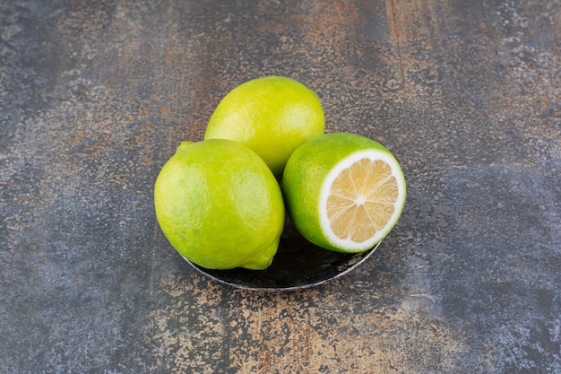 Limoni verdi in un piattino metallico su superficie rustica