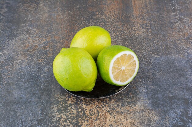 Green lemons in a metallic saucer on rustic surface