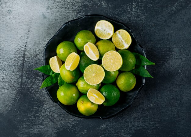 Green lemons in a plate with slices top view on a black textured background