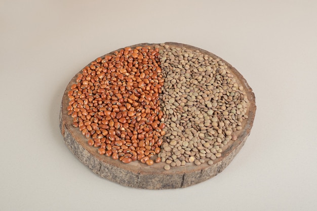 Green lentils and brown beans on a wooden board.