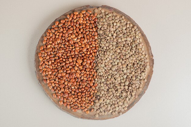 Green lentils and brown beans on a wooden board.