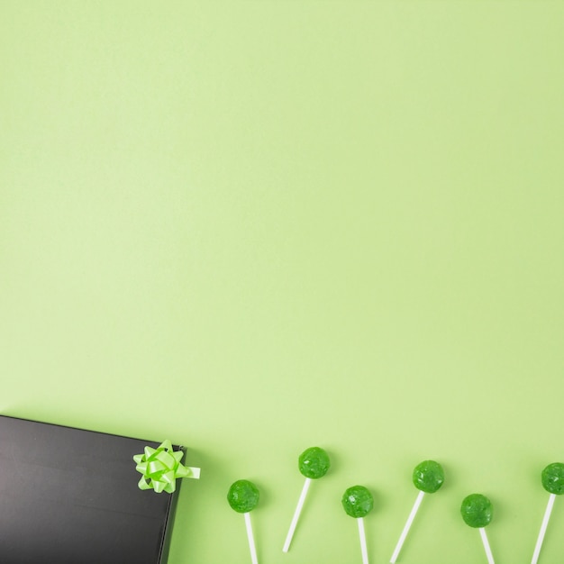 Green lollipops with black gift box and bow on green background