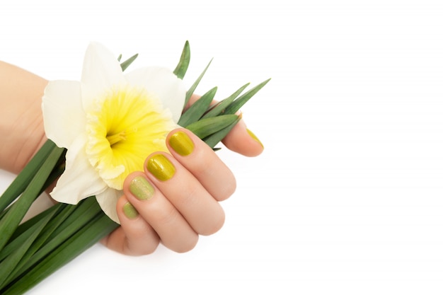 녹색 네일 디자인. 수 선화 꽃을 들고 반짝이 매니큐어와 여성 손.