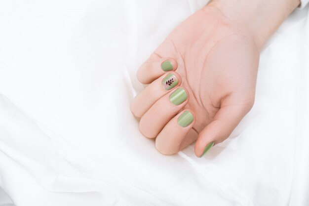 Green nail design with black tree art on middle finger. Manicured female hand