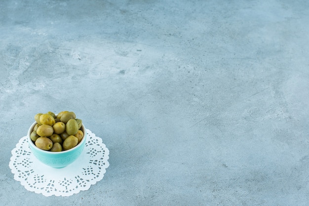 Free photo green olives in a bowl on a coaster , on the marble table.