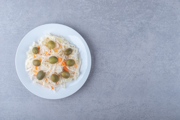 Free photo green olives on the sauerkraut on plate , on the marble background.