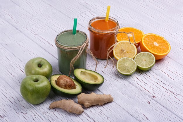 green and orange detox coctails stands on white table with fruits and vegetables