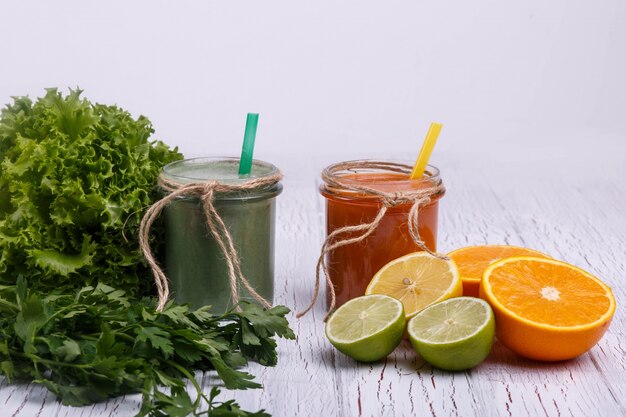 green and orange detox coctails stands on white table with fruits and vegetables