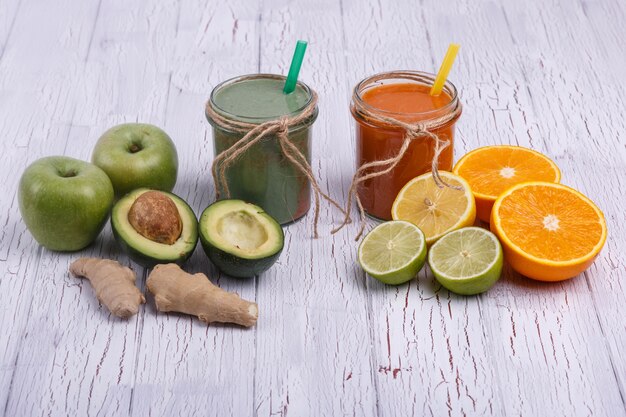 green and orange detox coctails stands on white table with fruits and vegetables