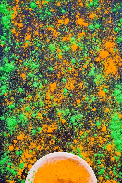 Green and orange holi powder splatter on black background