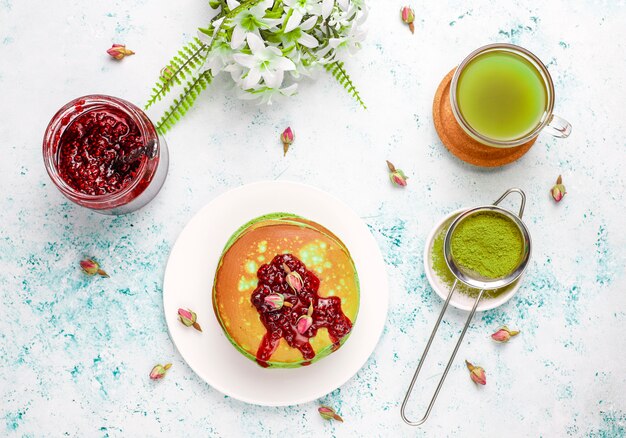 Green pancakes with matcha powder with red jam, top view